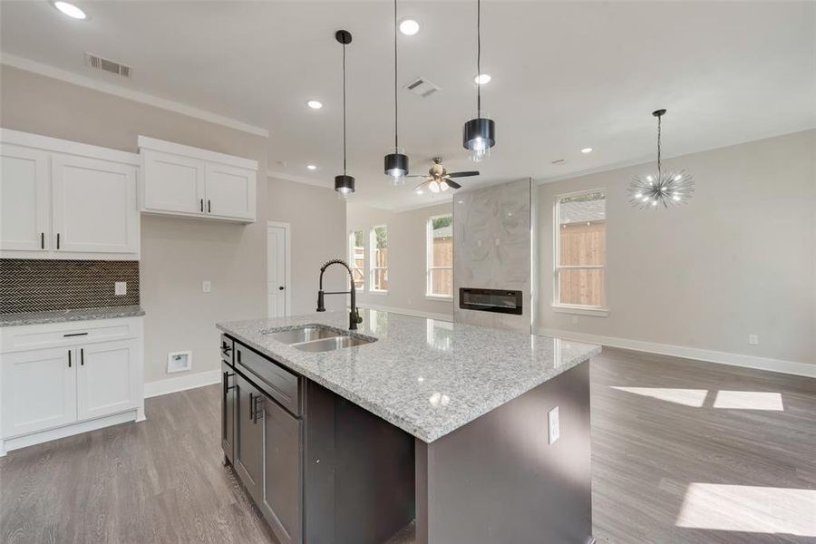 Kitchen featuring light hardwood / wood-style floors, a premium fireplace, ceiling fan with notable chandelier, hanging light fixtures, and sink