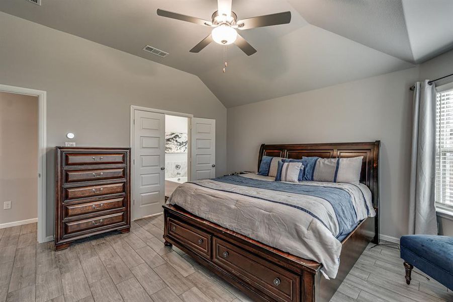 Bedroom with ensuite bath, vaulted ceiling, light hardwood / wood-style flooring, and ceiling fan