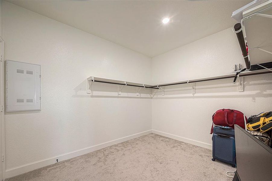 This is a neat and well-lit walk-in closet with built-in shelving and hanging rods, providing ample storage space.