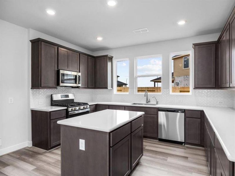 The kitchen showcases rich dark brown cabinets, granite countertops, and stainless steel appliances. An island adds extra workspace and seating, making it both stylish and functional.