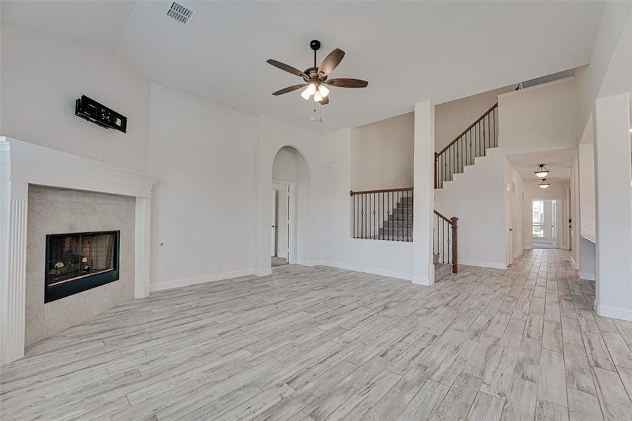 Unfurnished living room featuring a tile fireplace, light hardwood / wood-style flooring, high vaulted ceiling, and ceiling fan