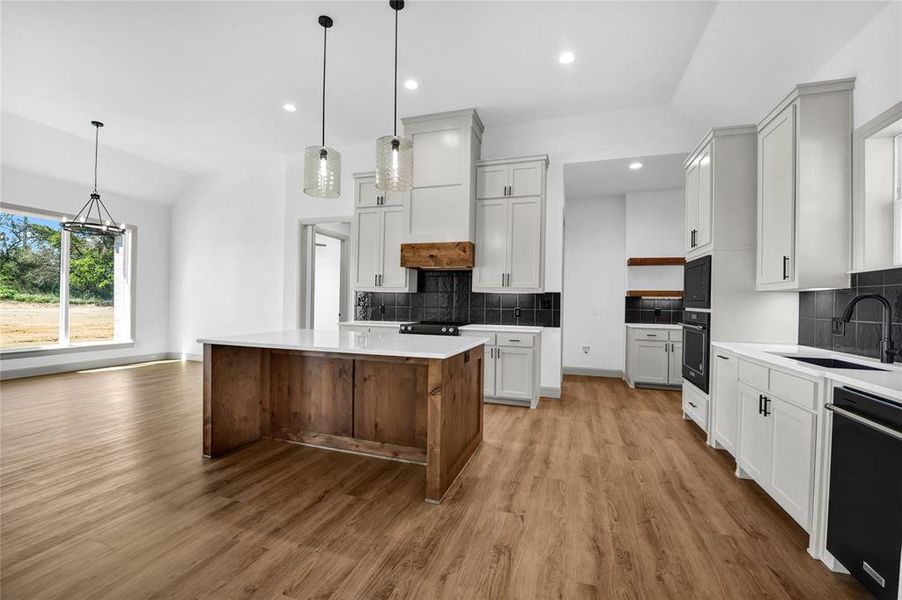 Kitchen featuring lofted ceiling, hanging light fixtures, sink, black appliances, and a center island