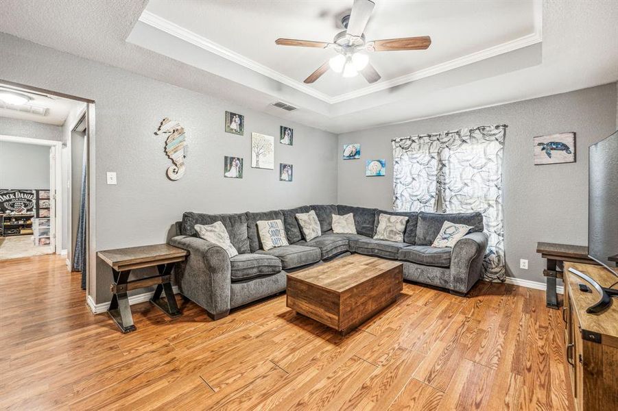 Living room with wood-type flooring, ornamental molding, and a tray ceiling