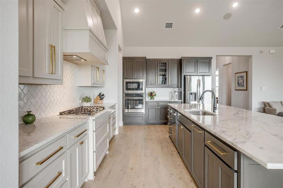 Kitchen featuring sink, stainless steel appliances, custom range hood, decorative backsplash, and light hardwood / wood-style flooring