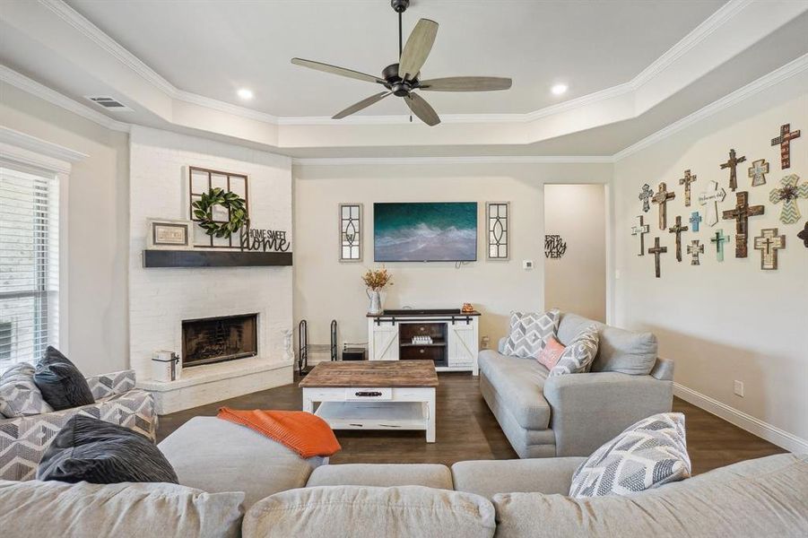 Living room with ceiling fan, ornamental molding, a tray ceiling, dark hardwood / wood-style floors, and a fireplace