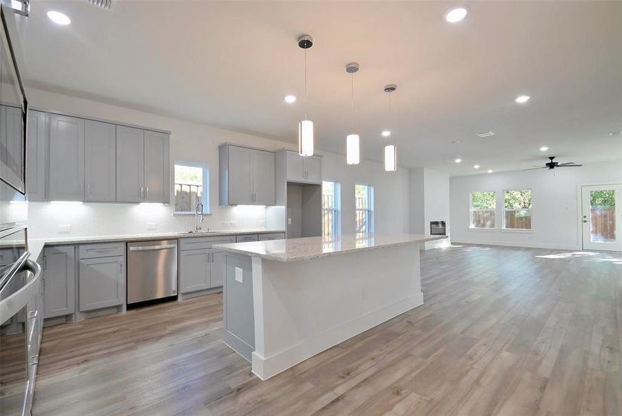 Kitchen with light stone counters, light wood-type flooring, a center island, decorative light fixtures, and stainless steel dishwasher