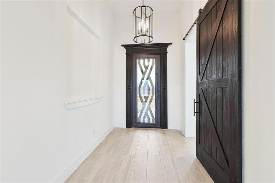 Foyer entrance with an inviting chandelier, light hardwood / wood-style floors, and a barn door