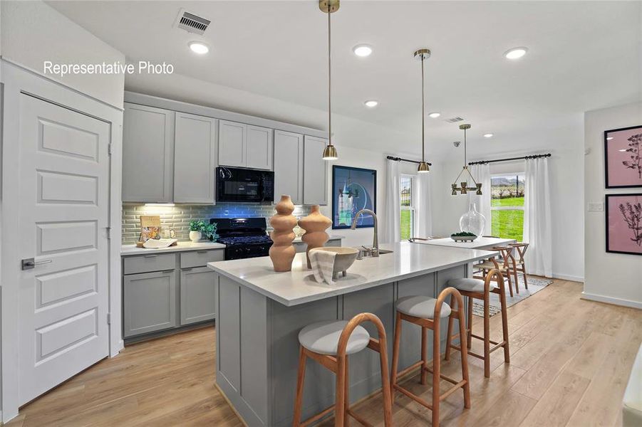 Kitchen featuring black appliances, hanging light fixtures, a center island with sink, gray cabinetry, and light hardwood / wood-style floors