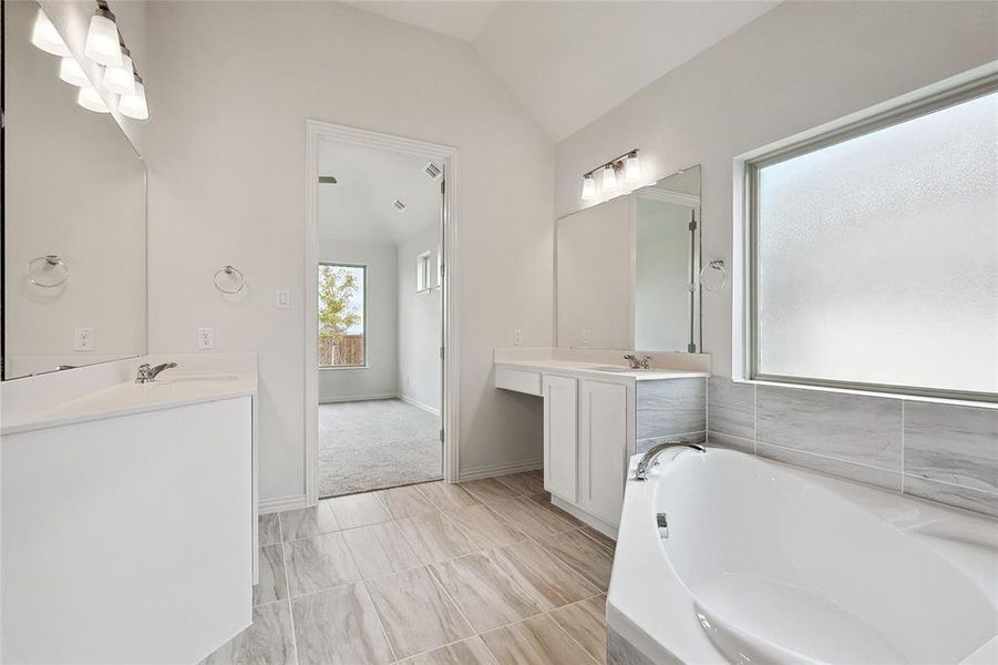 Bathroom featuring vaulted ceiling, a bath, and vanity