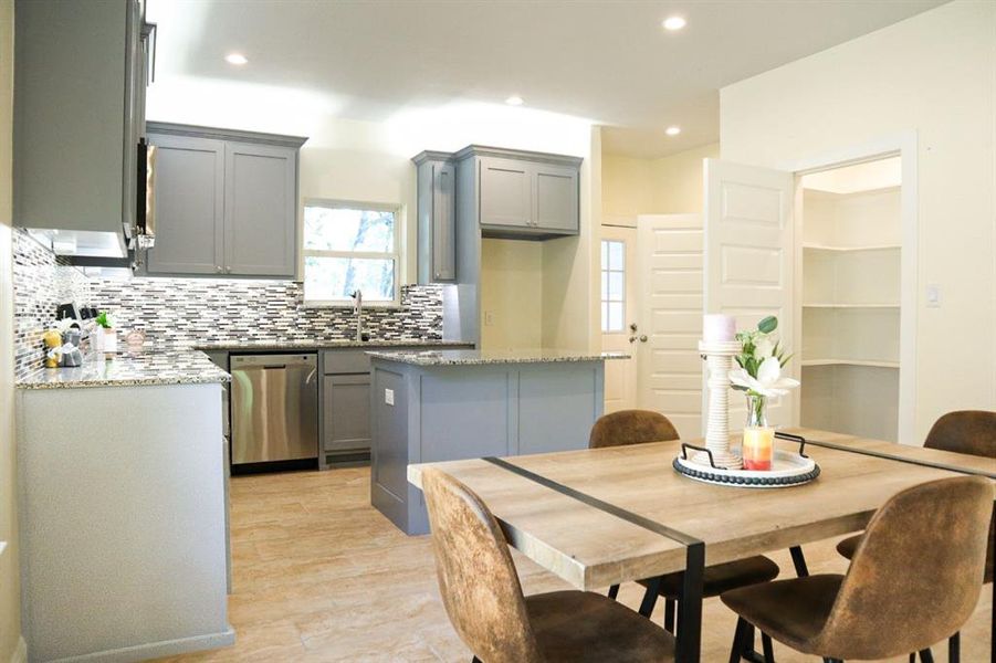 Kitchen featuring gray cabinets, dishwasher, light stone counters, and a kitchen island