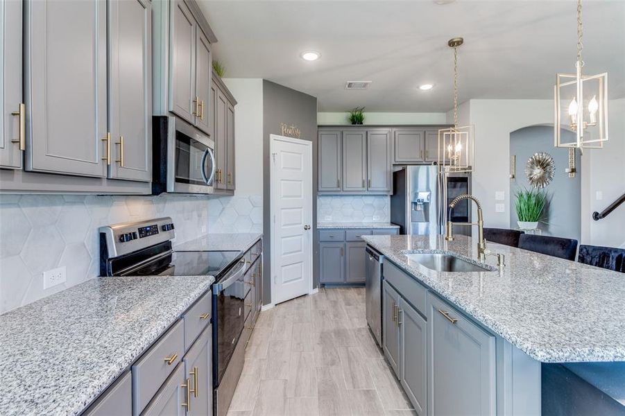 Kitchen with pendant lighting, sink, gray cabinetry, a center island with sink, and appliances with stainless steel finishes