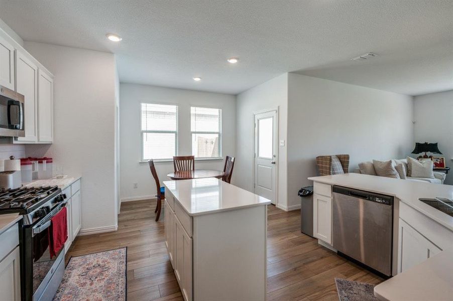 Kitchen with white cabinetry, a center island, stainless steel appliances, and hardwood / wood-style flooring