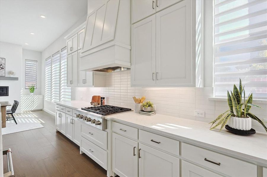 Kitchen featuring custom range hood, white cabinetry, stainless steel gas cooktop, light stone countertops, and dark hardwood / wood-style flooring