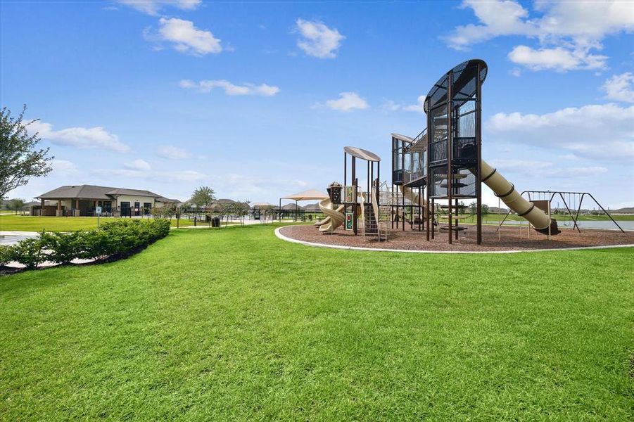 Spacious community area featuring a modern playground with slides and swings, lush green lawns, and a backdrop of residential buildings, perfect for families.