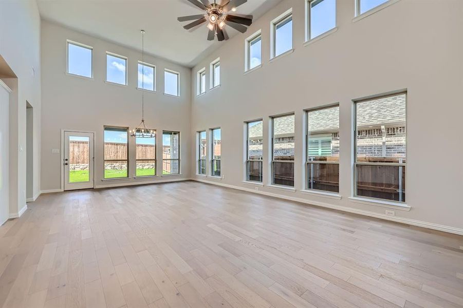 Living room featuring light hardwood / wood-style flooring, a healthy amount of sunlight, ceiling fan with notable chandelier, and a high ceiling