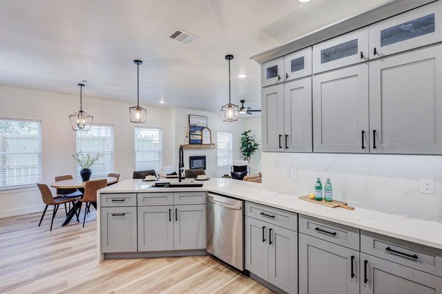 Kitchen with sink, light hardwood / wood-style floors, hanging light fixtures, gray cabinets, and dishwasher