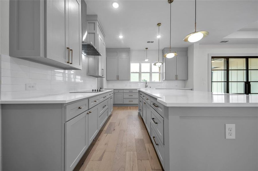 Kitchen with tasteful backsplash, wall chimney range hood, hanging light fixtures, light wood-type flooring, and gray cabinetry