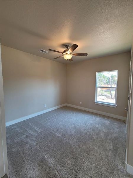 Carpeted empty room with ceiling fan and a textured ceiling