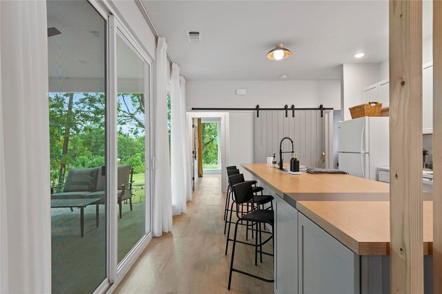 More natural light through the wall of windows. Kitchen featuring light wood-type flooring, a breakfast bar area and a barn door