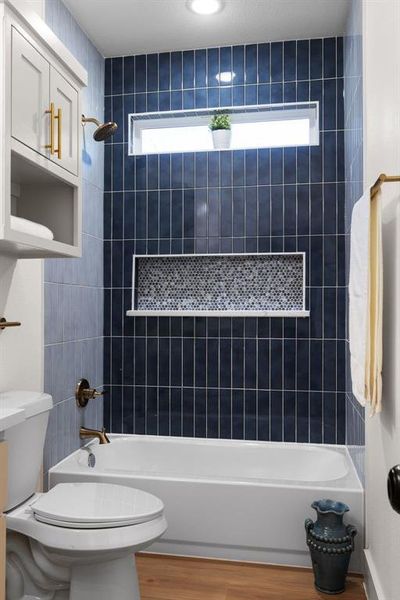 Bathroom with tiled shower / bath, plenty of natural light, toilet, and hardwood / wood-style flooring