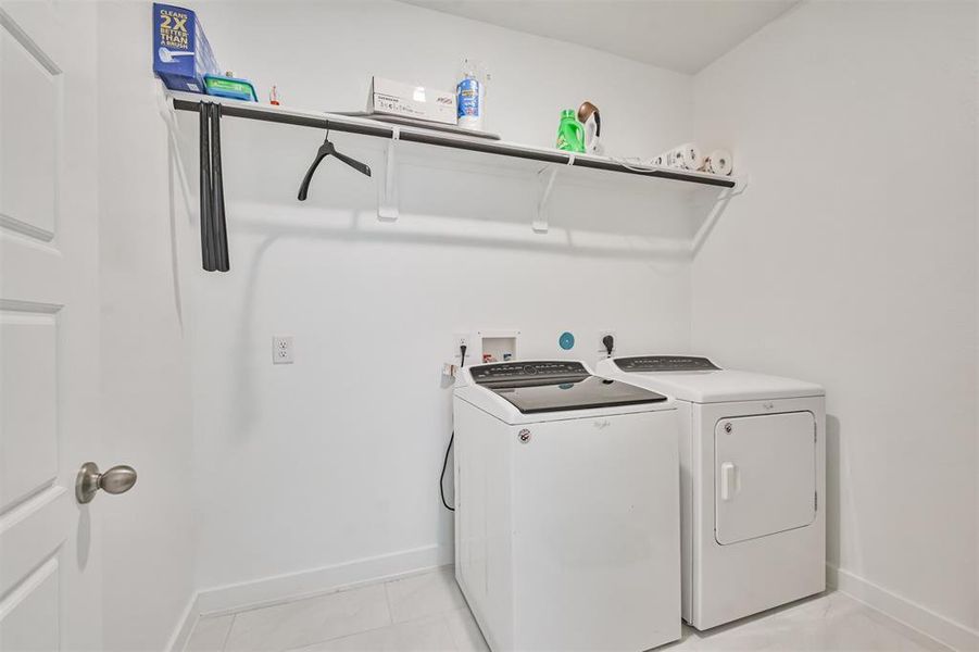 This is a neat, compact laundry room featuring a modern washer and dryer set with convenient overhead shelving for storage.
