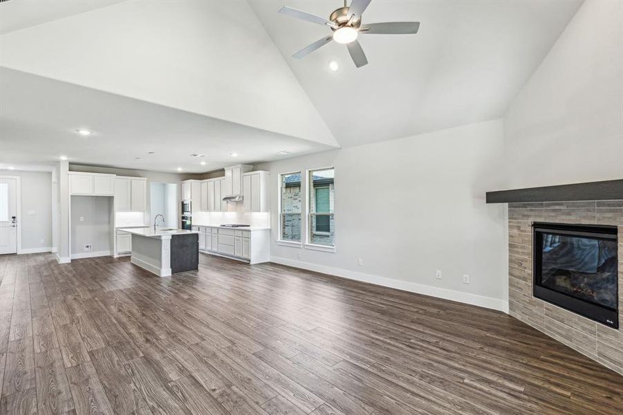 Unfurnished living room with a tile fireplace, wood-type flooring, sink, high vaulted ceiling, and ceiling fan