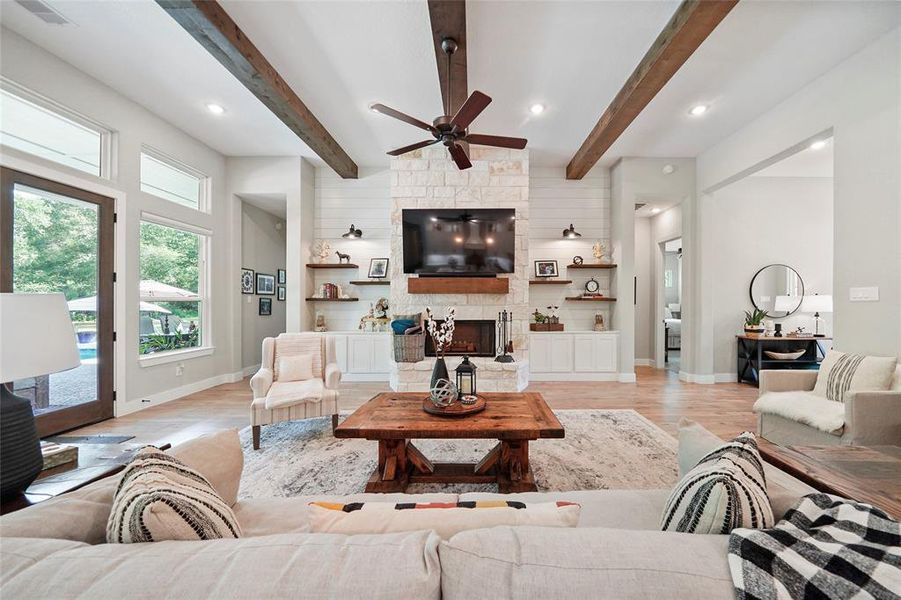 This stunning family room features exposed wood beams and a cozy stone gas-log fireplace set against a ship-lap wall with custom lighting and shelving. The wall of windows and glass doors offer beautiful views of the pool, seamlessly connecting indoor and outdoor living. Open to the spacious island kitchen, this area is perfect for entertaining and family gatherings. Enjoy the blend of comfort and elegance in this well-designed space.