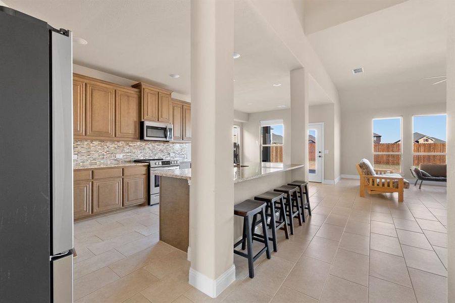 Kitchen with light stone countertops, light tile patterned floors, appliances with stainless steel finishes, tasteful backsplash, and a kitchen bar