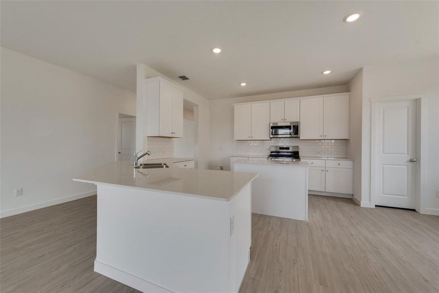 Kitchen featuring white cabinetry, backsplash, light hardwood / wood-style floors, appliances with stainless steel finishes, and sink