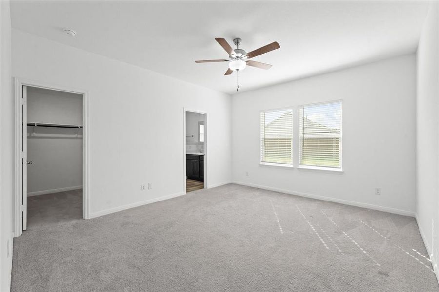 Unfurnished bedroom featuring ceiling fan, connected bathroom, light colored carpet, and a walk in closet