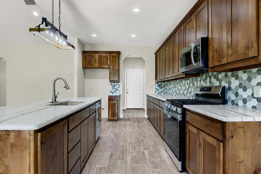 Kitchen featuring decorative backsplash, stainless steel appliances, a kitchen island with sink, and sink