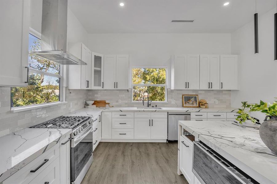 Kitchen featuring appliances with stainless steel finishes, wall chimney exhaust hood, white cabinets, and light hardwood / wood-style flooring