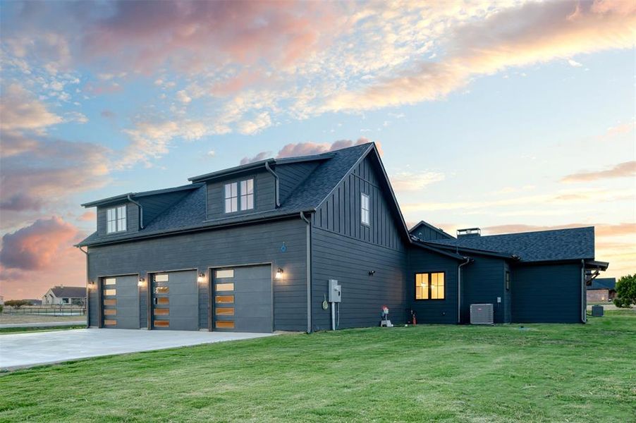 Property exterior at dusk featuring a yard, central air condition unit, and a garage