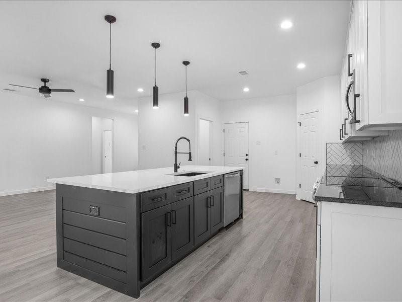 Kitchen featuring white cabinetry, ceiling fan, decorative backsplash, light wood-type flooring, and a kitchen island with sink