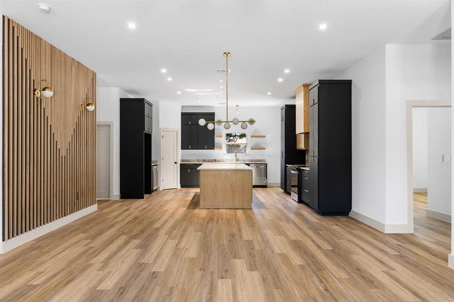 Kitchen with light hardwood / wood-style flooring, a center island, appliances with stainless steel finishes, and decorative light fixtures