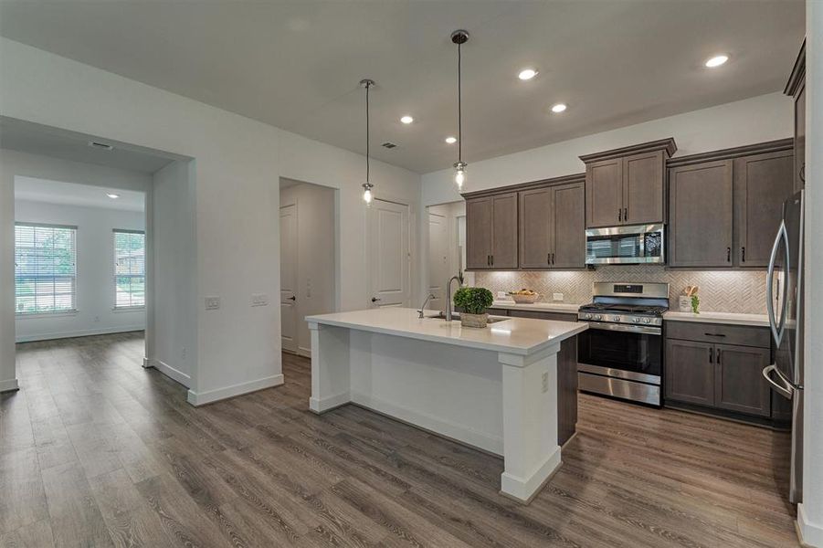 Stunning quartz countertop island with breakfast bar, upgraded backsplash, designer lighting, and stylish cabinetry. Note the beautiful lines in this floor plan.