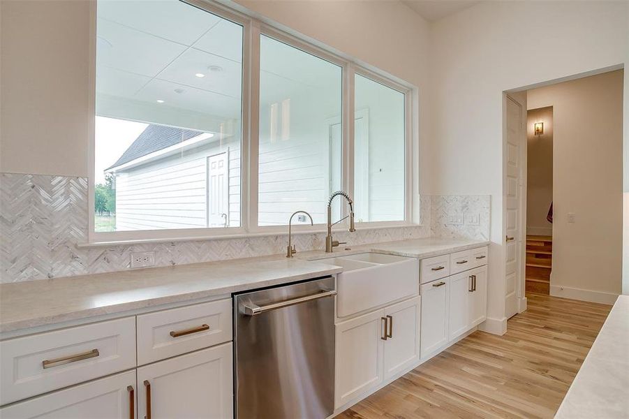 Kitchen featuring stainless steel dishwasher, white cabinetry, tasteful backsplash, sink, and light hardwood / wood-style flooring