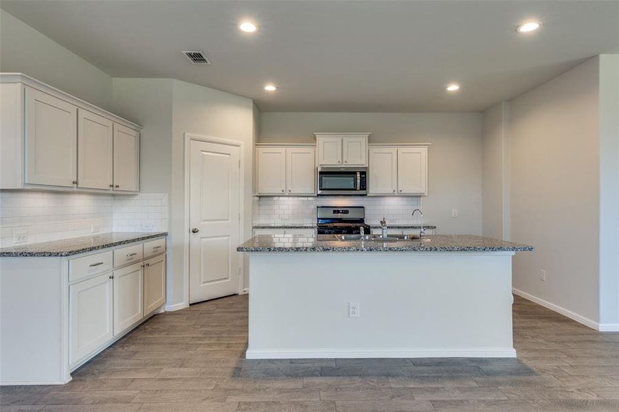 Kitchen with a center island with sink, appliances with stainless steel finishes, light hardwood / wood-style floors, and white cabinetry