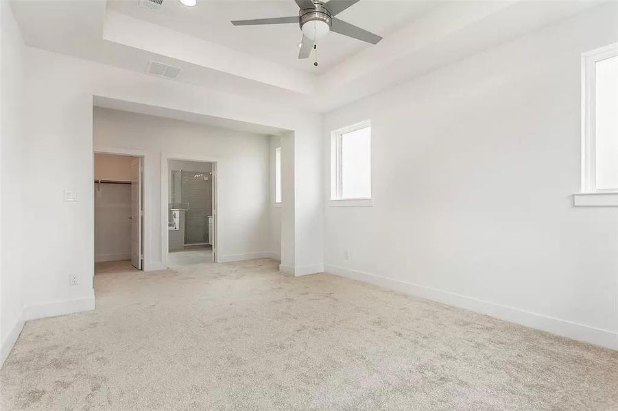 Unfurnished bedroom featuring carpet flooring, ceiling fan, a spacious closet, and a tray ceiling