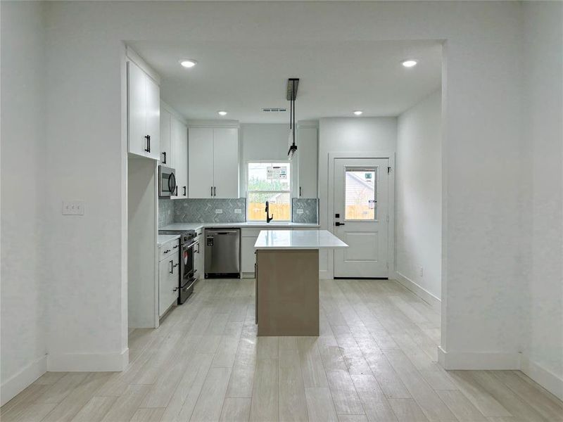 Kitchen featuring white cabinets, a kitchen island, light hardwood / wood-style flooring, pendant lighting, and stainless steel appliances