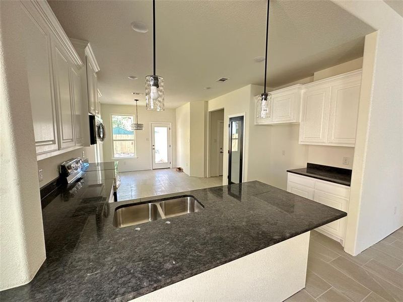 Kitchen featuring sink, white cabinets, hanging light fixtures, and dark stone countertops