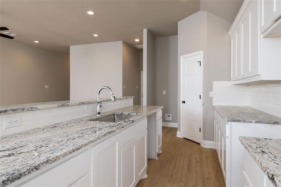 Kitchen featuring white cabinetry, light wood-type flooring, light stone countertops, decorative backsplash, and sink