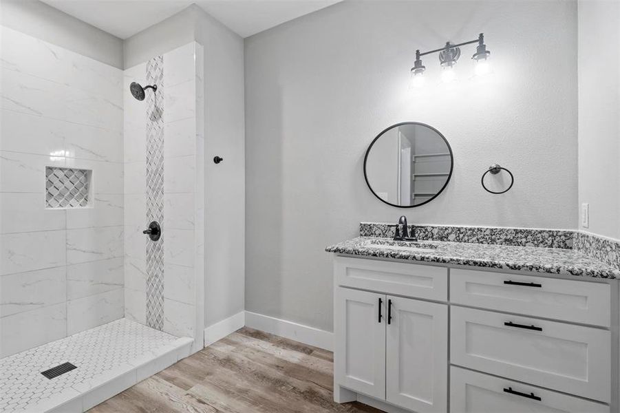 Bathroom featuring tiled shower, hardwood / wood-style flooring, and vanity with extensive cabinet space