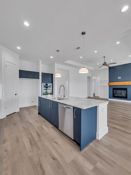 Kitchen with a large fireplace, hanging light fixtures, a large island with sink, light wood-type flooring, and stainless steel appliances