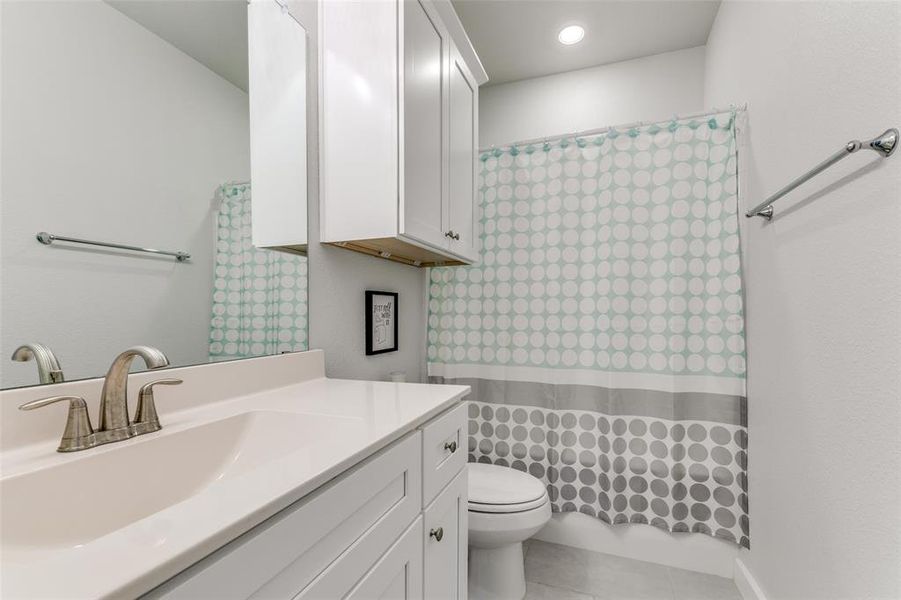 Secondary bathroom featuring walk in shower, vanity, tile patterned flooring, and toilet