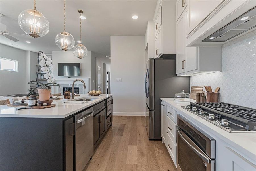 Kitchen with light wood-type flooring, custom range hood, stainless steel appliances, white cabinets, and backsplash