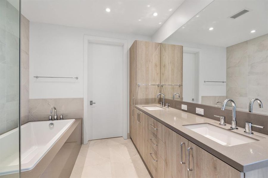 Primary en-suite bathroom with dual vanities, soaking tub and porcelain tiles.