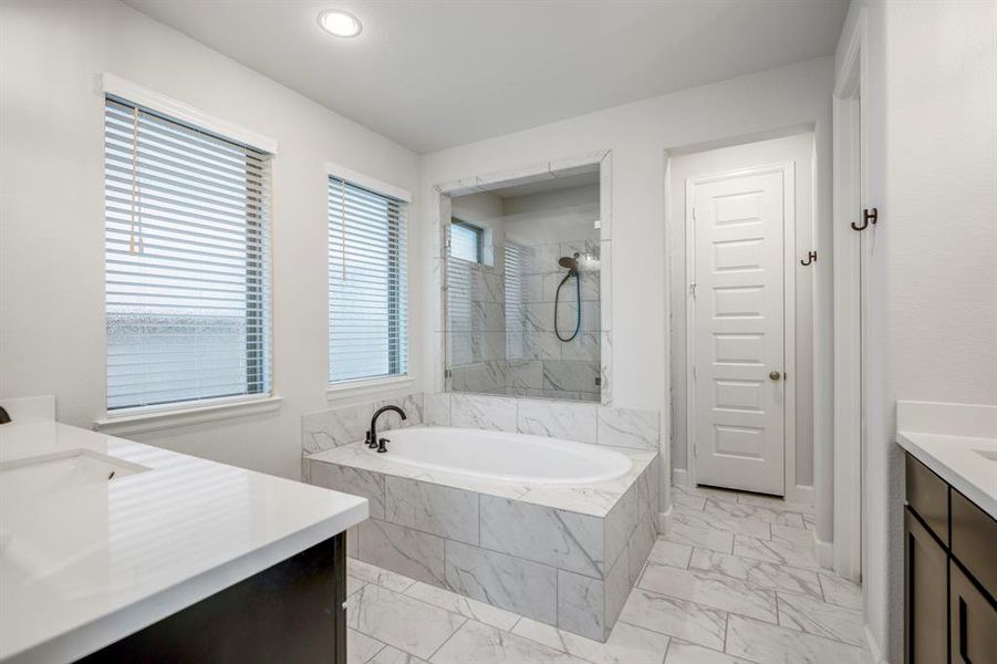 You'll love getting ready in this light and bright primary bathroom! The primary bathroom has a large walk-in shower with a marbled tile surround, glass door, and window for lighting, and it includes a large soaking tub, perfect for relaxation.