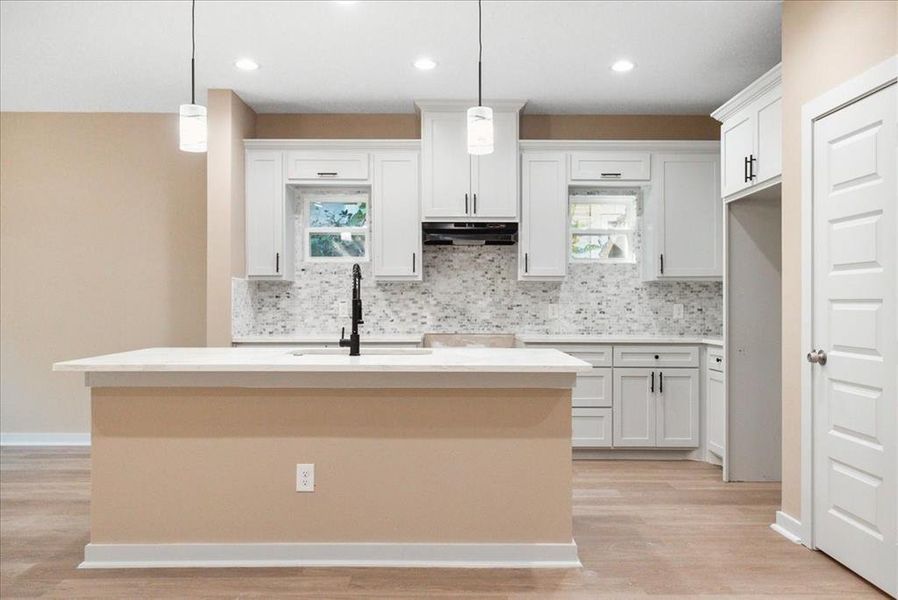 Kitchen featuring light hardwood / wood-style floors, sink, a kitchen island with sink, white cabinetry, and decorative light fixtures