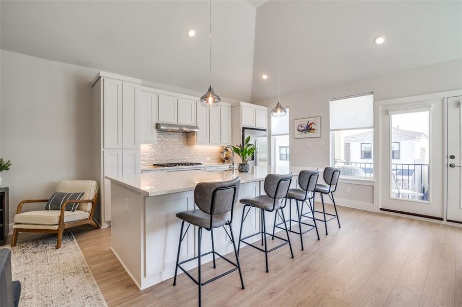 Kitchen featuring a spacious island, white cabinets, stainless appliances, and pendant lights.